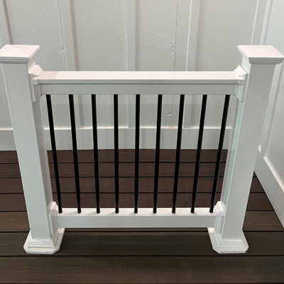 A deck rail sample at Ladiesburg Lumber, it is white framed with black rod guards - topped with a white piece of lumber.