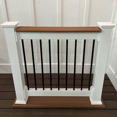 A deck rail sample at Ladiesburg Lumber, it is white framed with black rod guards - topped with a dark brown piece of lumber.