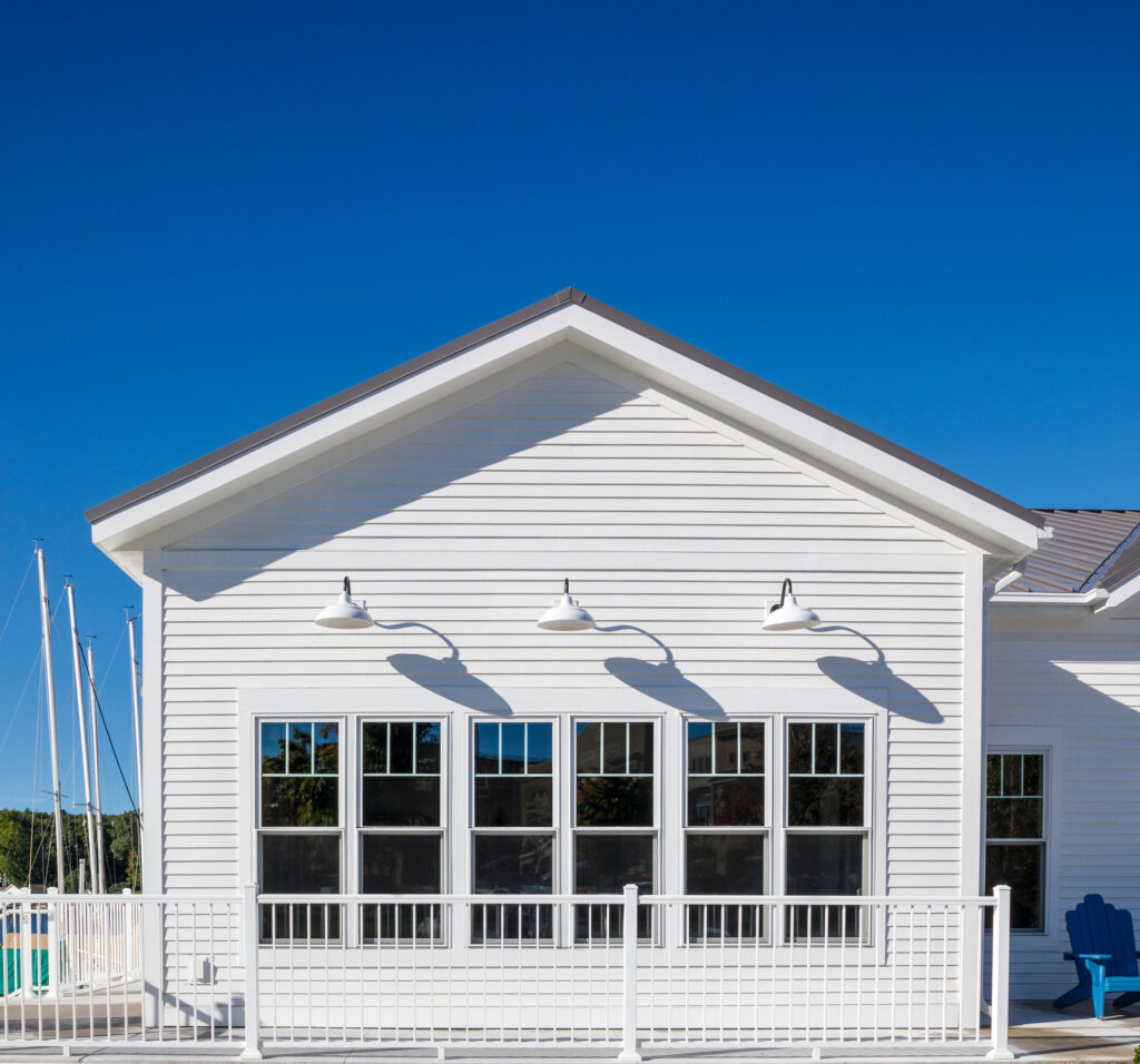 A white boathouse with blue accent Adirondack chair off to the right.
