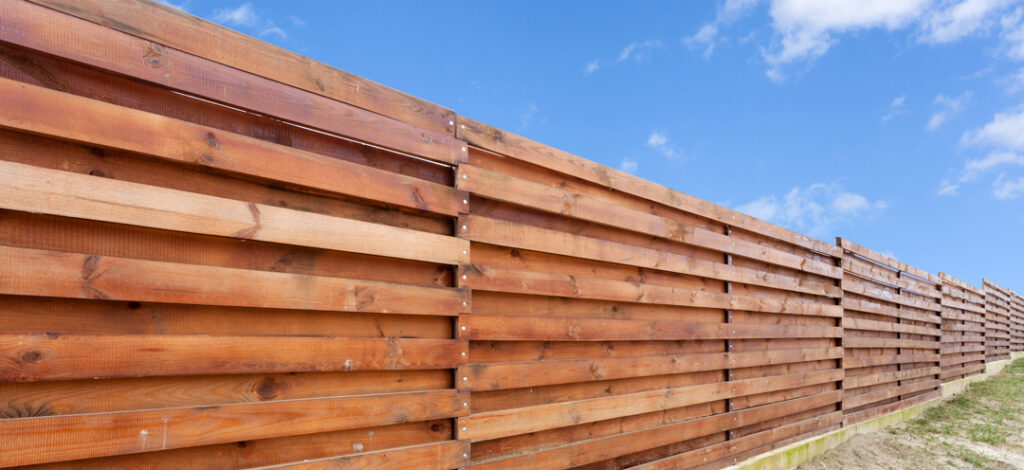 Long wooden cedar fence against blue sky.
