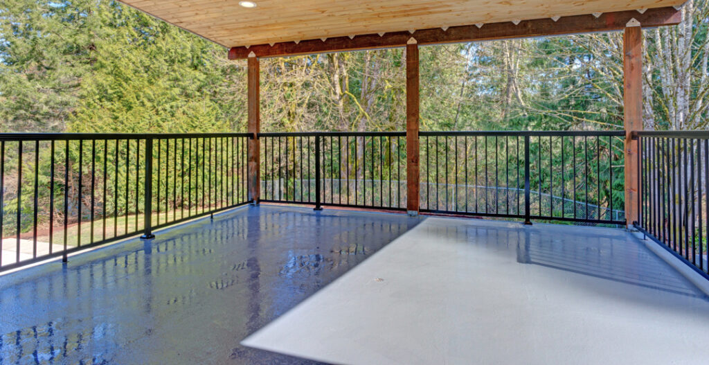 An outdoor, covered deck featuring recessed lighting, black metal fencing, and lumber posts supporting the frame.