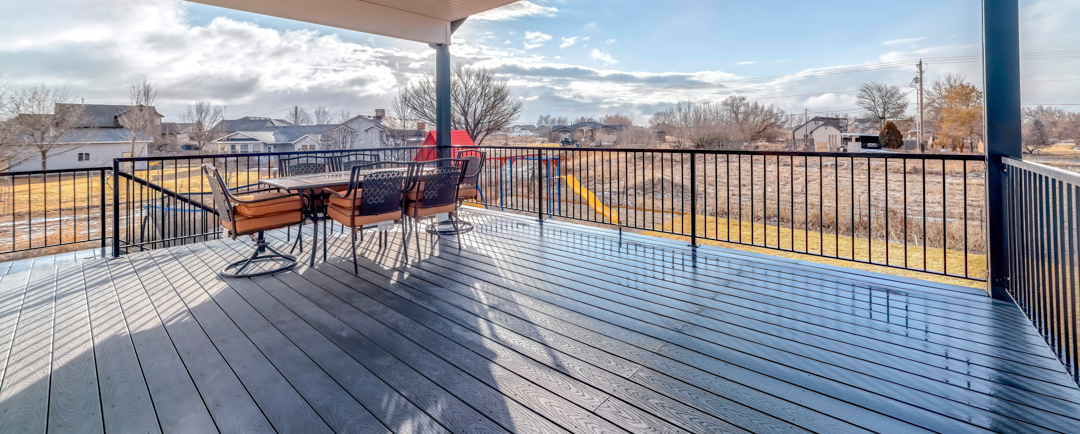 Dining table chairs and ceiling fan with light on wooden deck with metal railing.