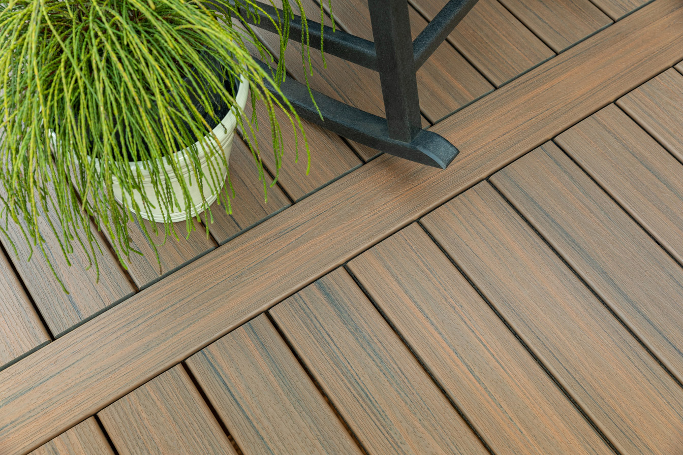 A close up shot of a dark brown deck featuring a potted plant and rocking chair.