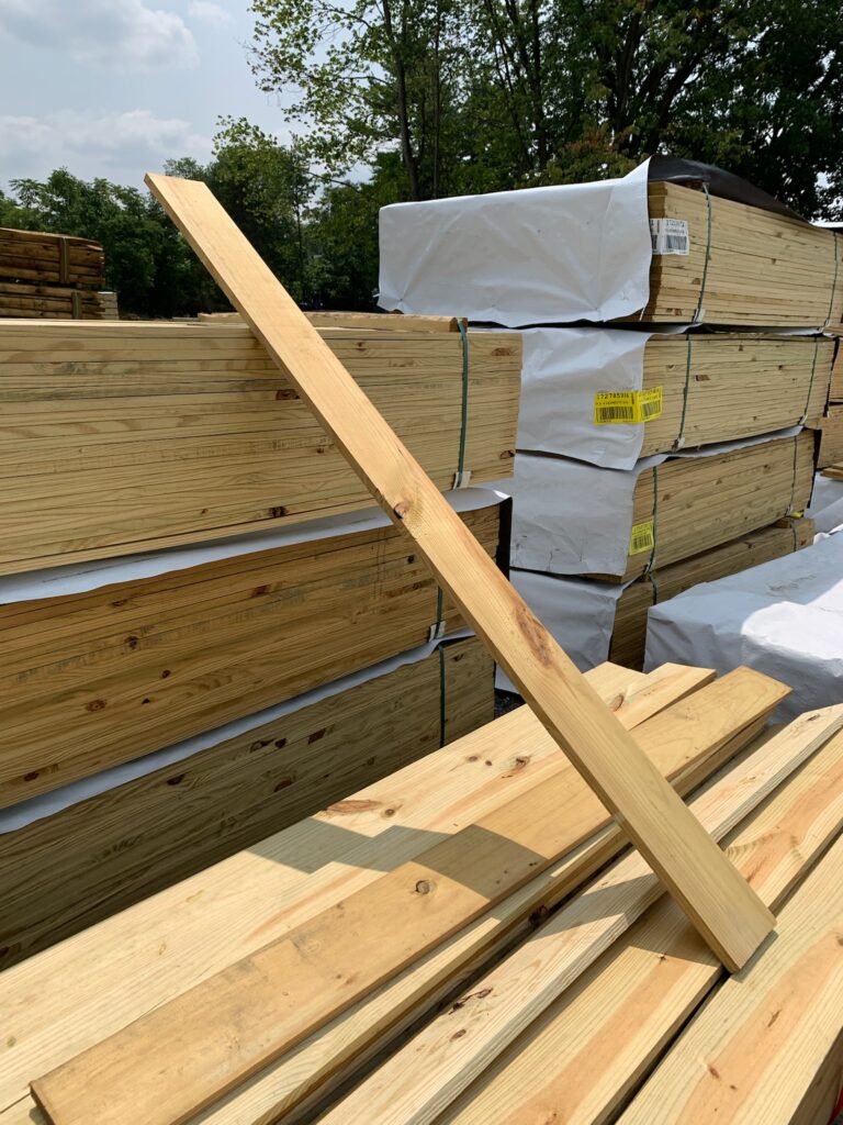 A 2x6 piece of lumber sitting against larger stacks of pressure treated wood.