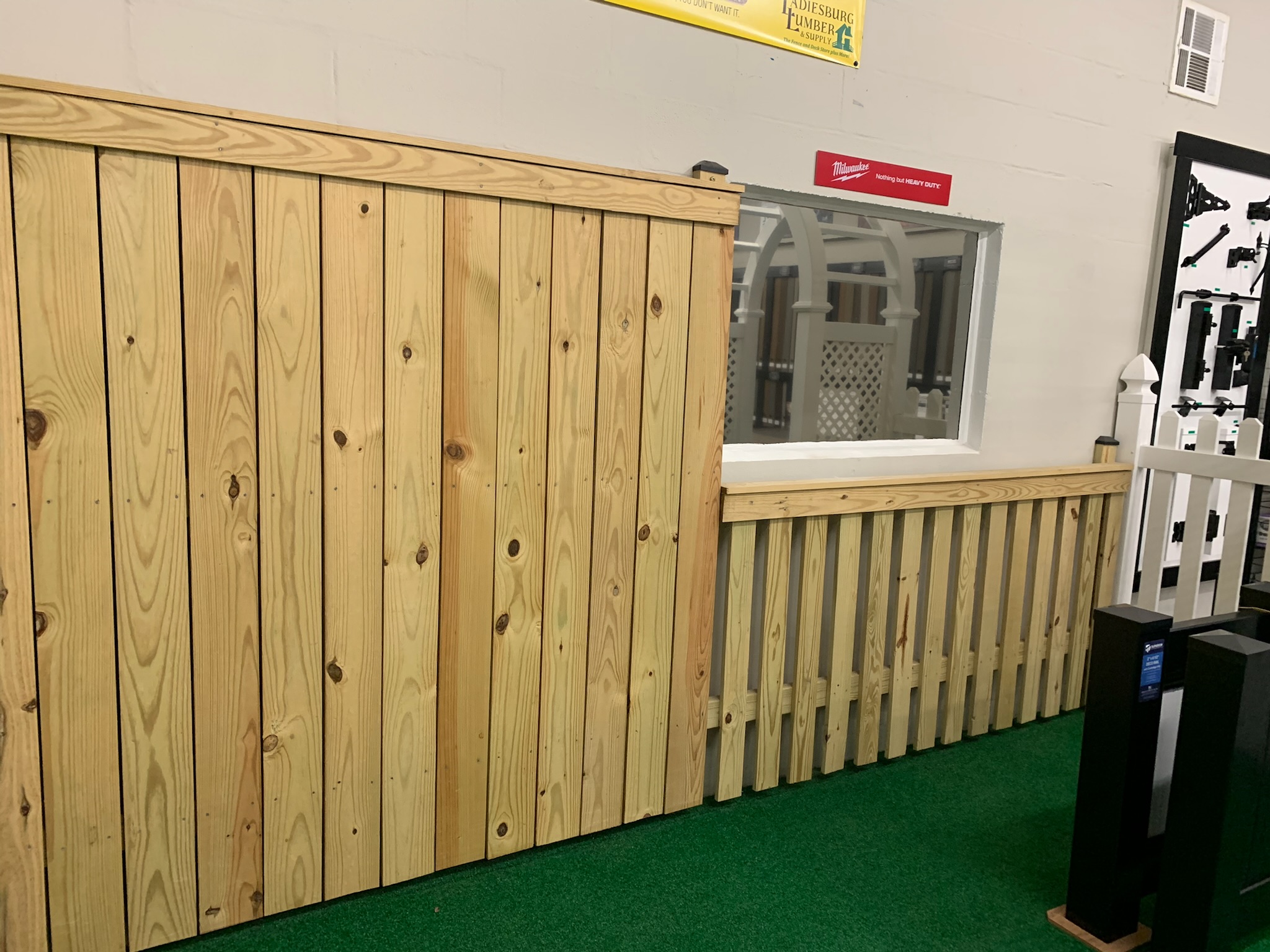In store wooden fence displays, one tall privacy fence stands next to a shorter, waist level dividing fence.