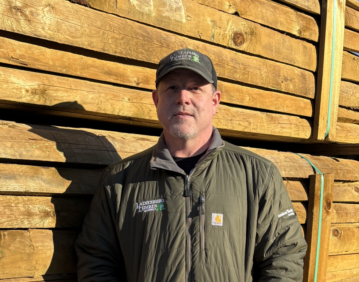 Jason McKenzie (Warehouse Operations Supervisor) standing for a headshot in front of a large stack of lumber.