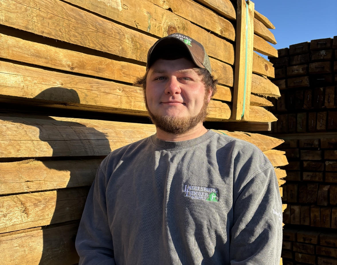 Allen Speak (Warehouse & Delivery Manager) standing for a headshot in front of a large stack of lumber.