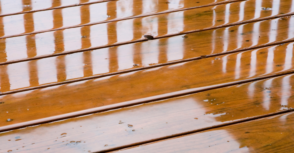 A wet deck close up, you can see the reflection of the railing the water.