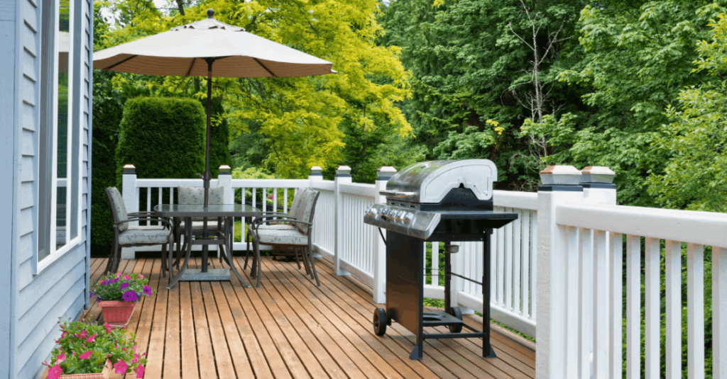A beautiful back deck with grill front & center and umbrella covered table in the distance.