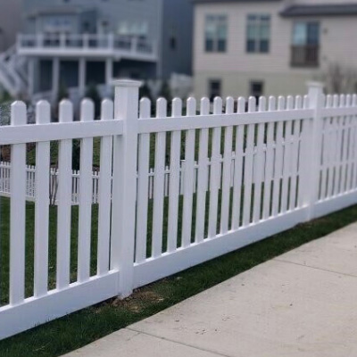 A small white picket fence adjacent to a sidewalk.