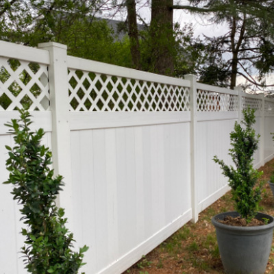 A tall white privacy fence with lattice cut tops, there are two potted plants in front.