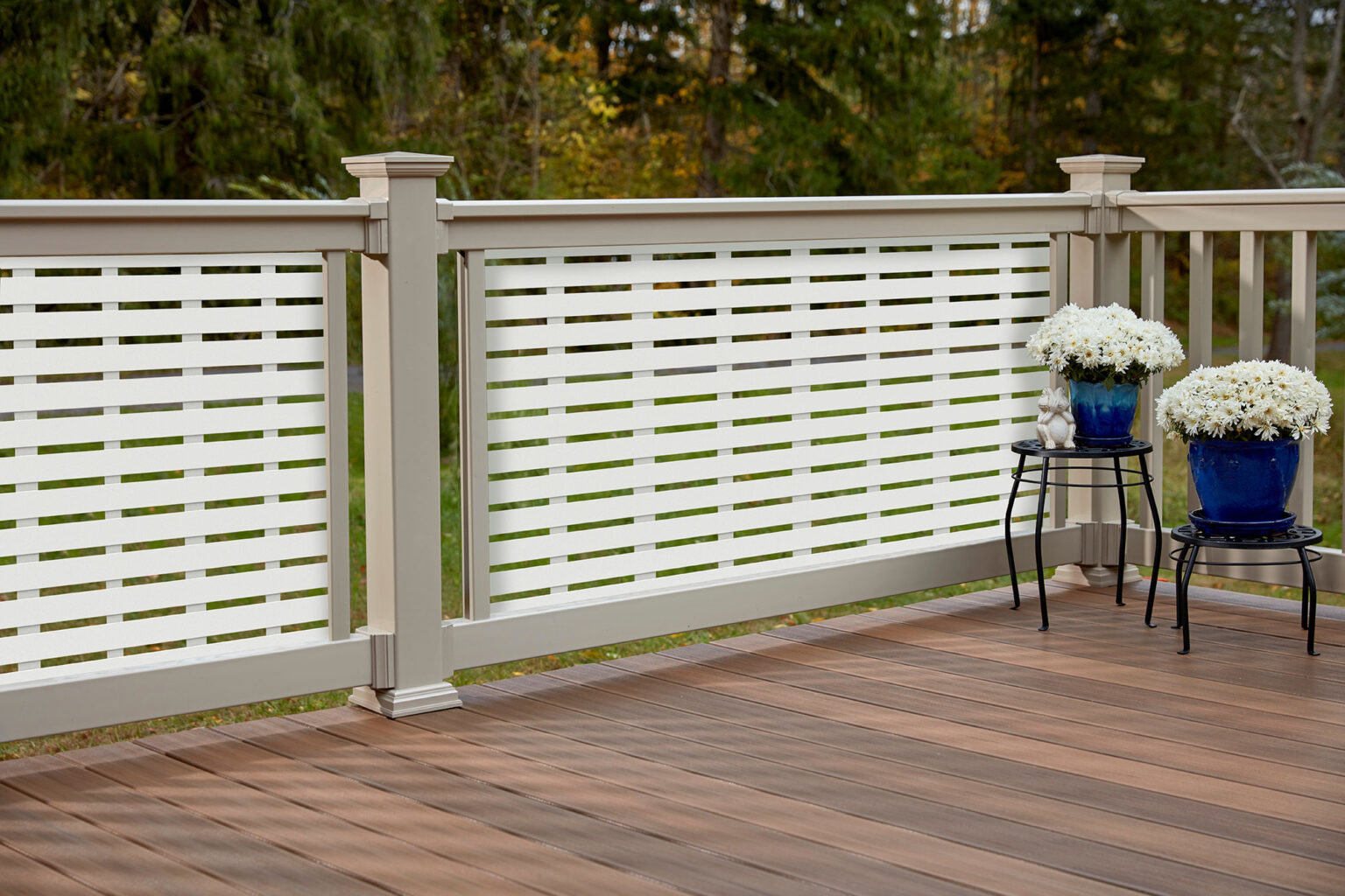 On a modern deck featuring beige deck railings, white cross cut rail guards, and potted plants off to the right.