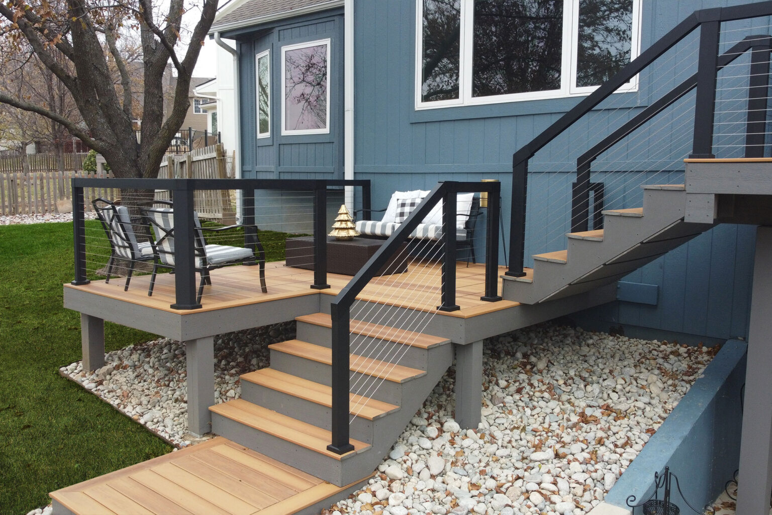 A back patio featuring a gray framed deck, light brown decking, and black metal wire railings.