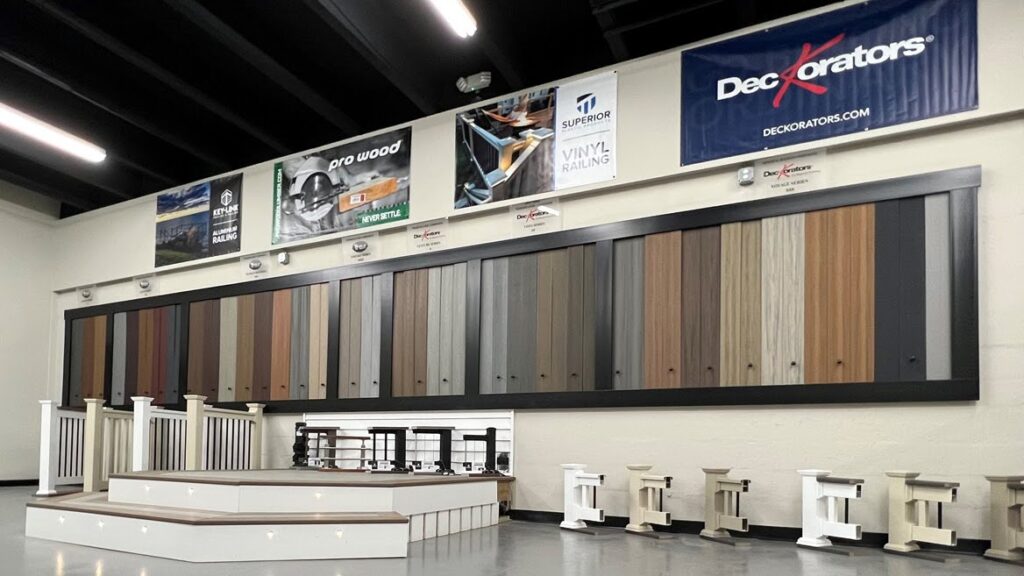 Inside the Ladiesburg Lumber showroom, there are samples of composite decking on the wall, deck fence cross sections on the right side of the floor, a small step up with built in lights towards the left, and more deck fence samples to the left of the photo.