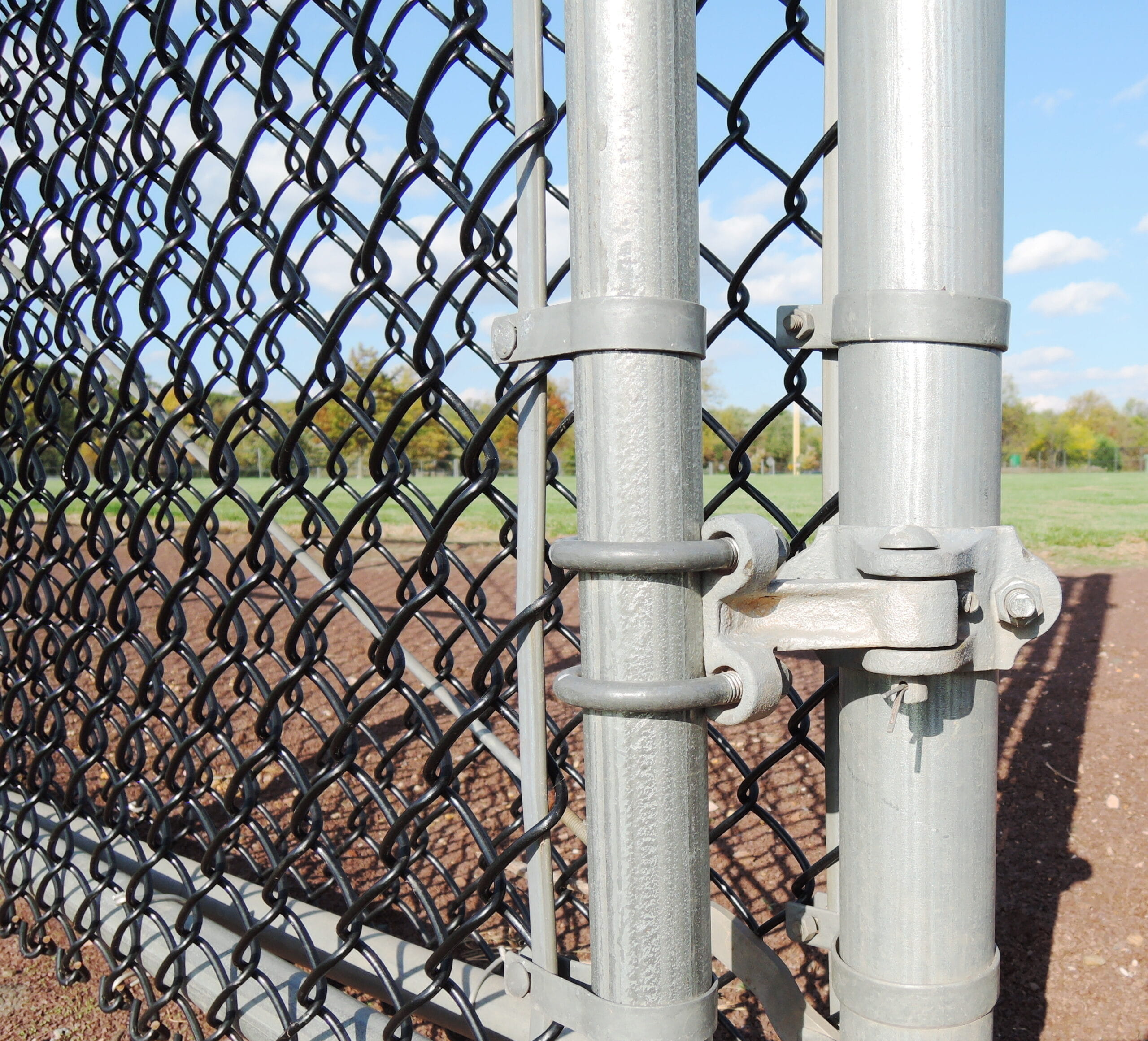 An up close shot of an aluminum chain link fence next to a sports field.