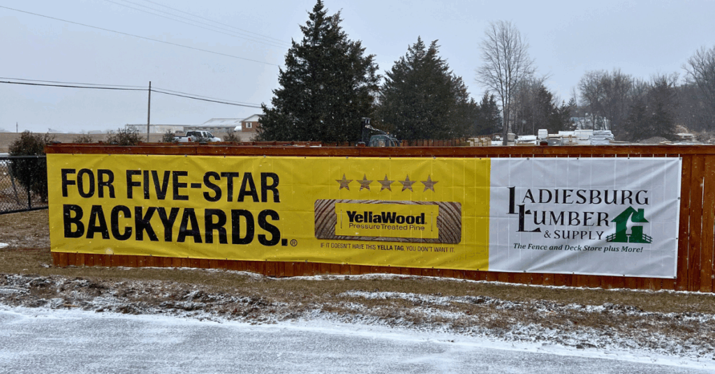An outdoor banner display featuring a large graphic for YellaWood (supplied at Ladiesburg Lumber).