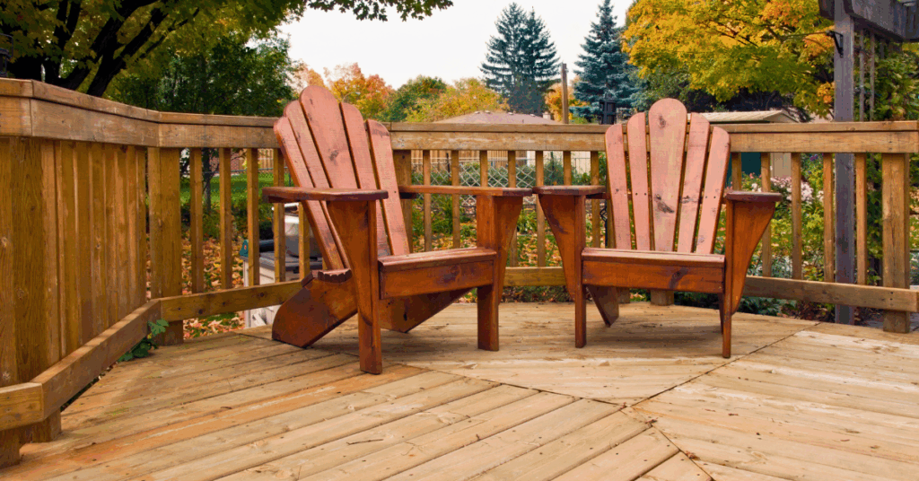 Two Adirondack chairs butt up against a wooden deck railing, ready to enjoy the fall weather.