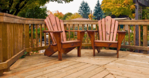 Two Adirondack chairs butt up against a wooden deck railing, ready to enjoy the fall weather.