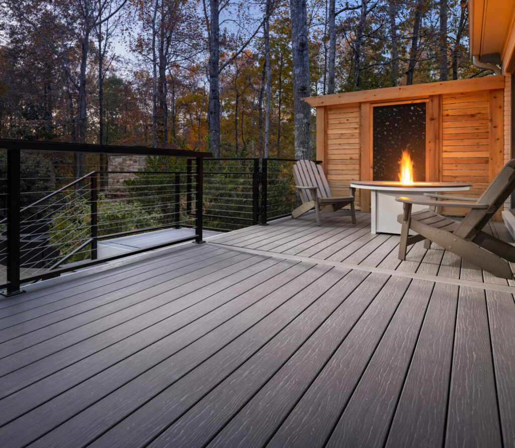 A beautifully designed and manufactured deck featuring a fire pit, Adirondack chairs, composite decking materials, and black aluminum fence.