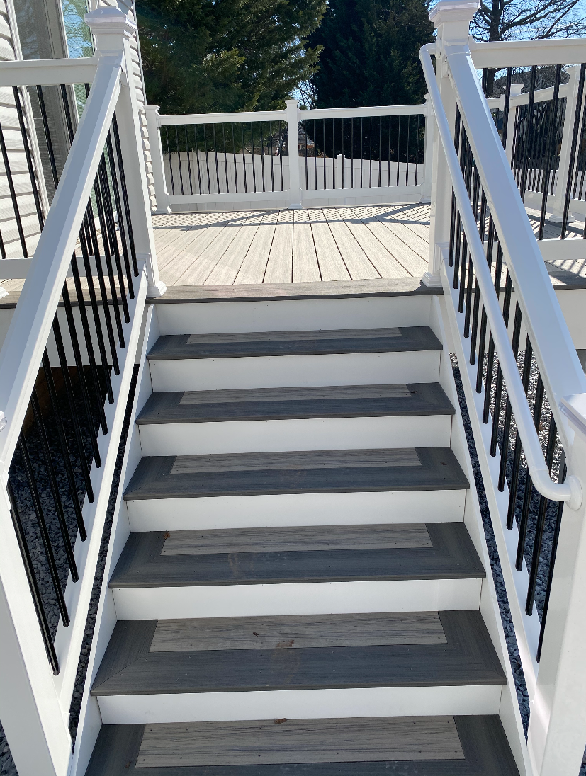 A white framed deck with gray stairs leading up to the house.