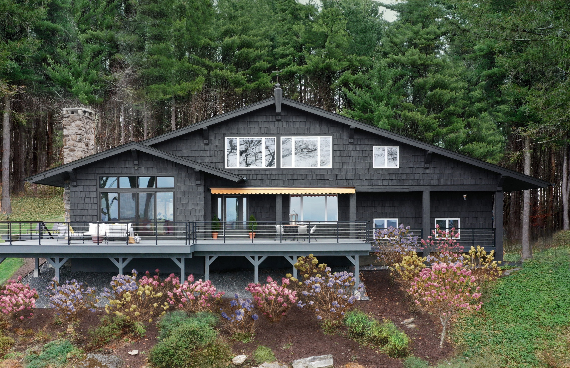 A black modern Craftsman styled home sits on a sloped hill in a wooded area.