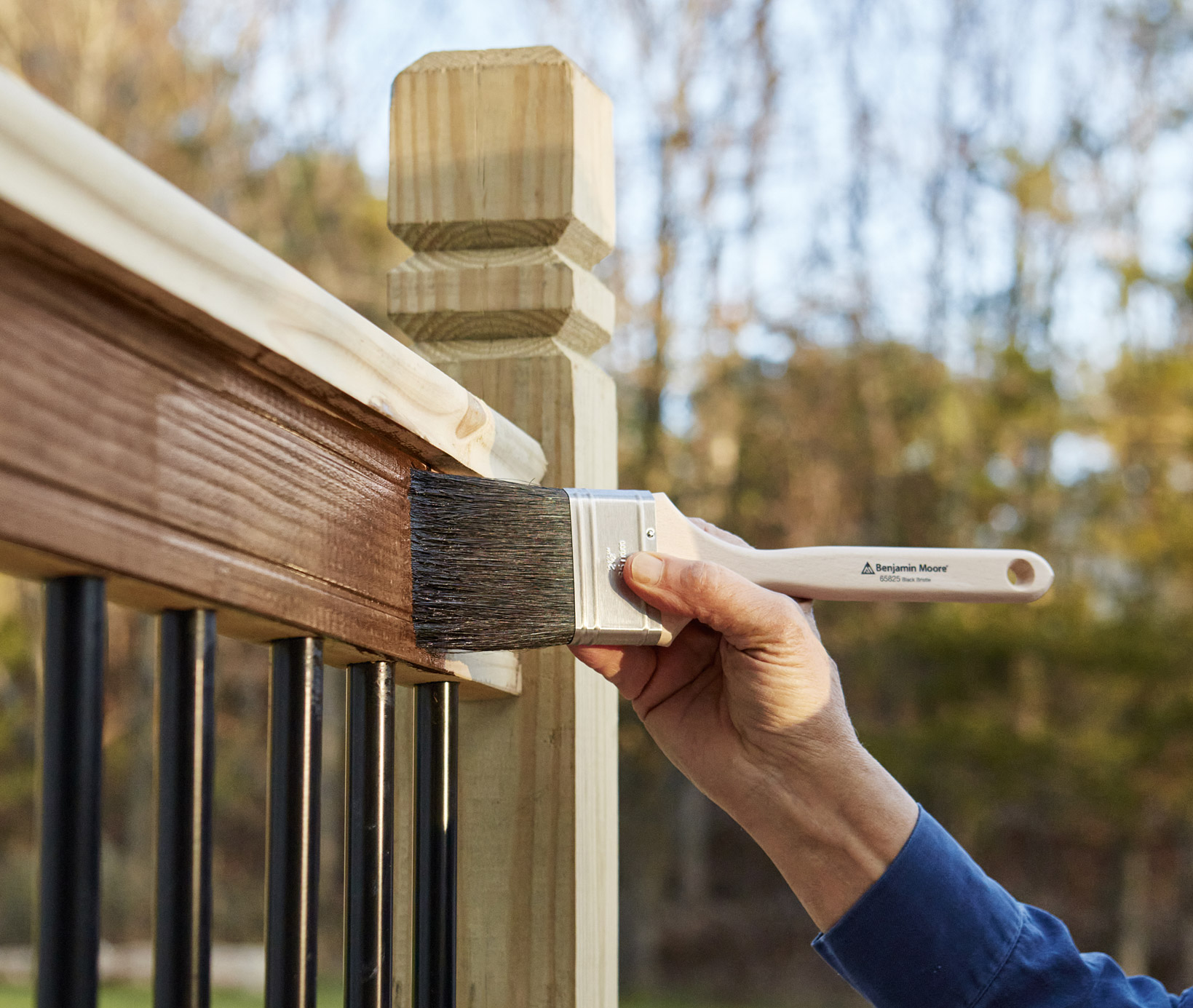 A Benjamin Moore ad featuring a painter brushing on sealant onto a lumber railing.